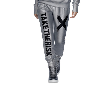 Person wearing silver jogger pants with 'TAKE THE RISK' text and black X, standing on a white background.